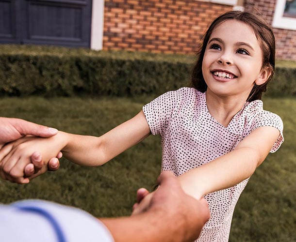 little girl holding fathers hands in yard
