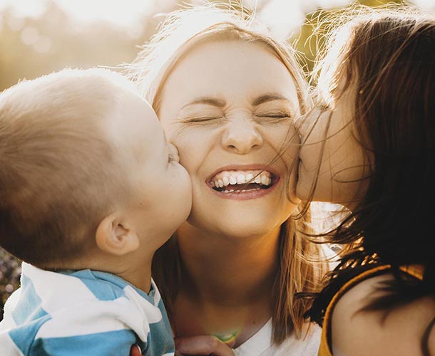 two children kissing moms cheeks